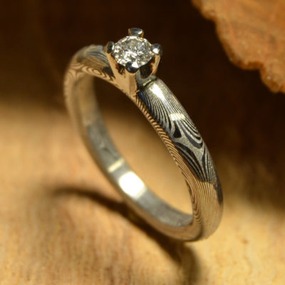 Prsten z nerezové damaškové oceli, briliant 0,16 ct SI/G(3,5 mm)zasazený ve zlatě 750/1000.