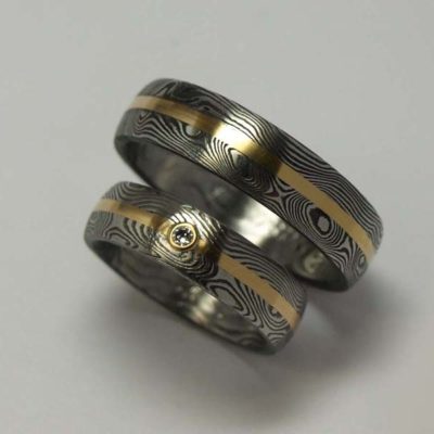 Snubní prsteny z damaškové nerez oceli, doplněné pruhy z 18. karátového žlutého zlata a briliantem 2 mm kvality G/Si.